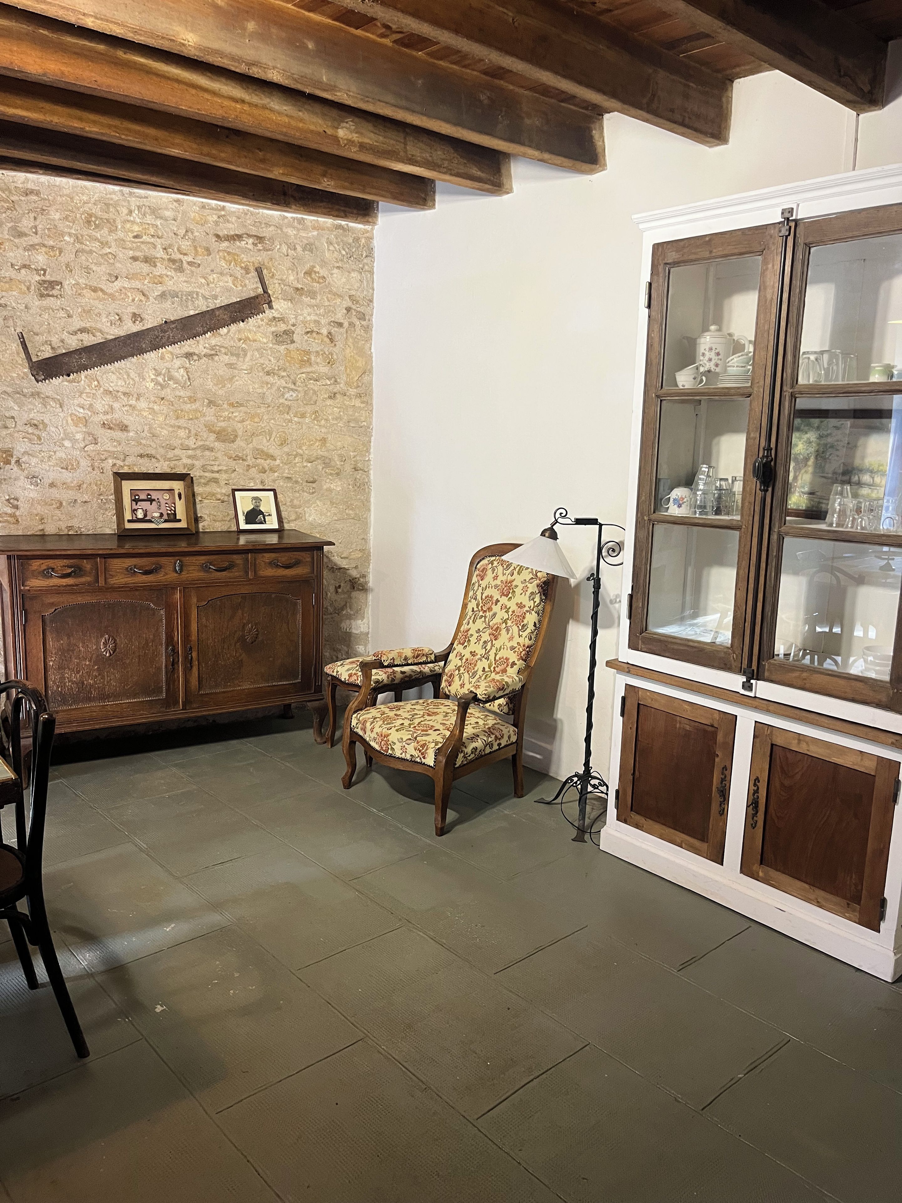 A room with a stone wall, wooden furniture, a cabinet with glass doors, and a chair with floral upholstery.