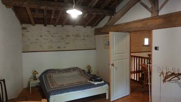 Een slaapkamer met een houten plafond, een bed met een bedovertrek met dessin, een nachtkastje met een lamp en een deur die leidt naar een balkon.