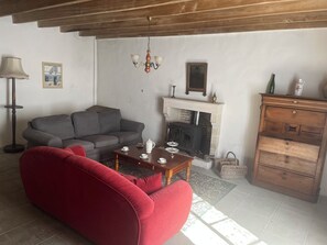 A living room with a sofa, a red chair, a wooden table with tea set, a fireplace, and a wooden cabinet. - Gite Chez Robin in the Deux-Sèvres (Ardin)