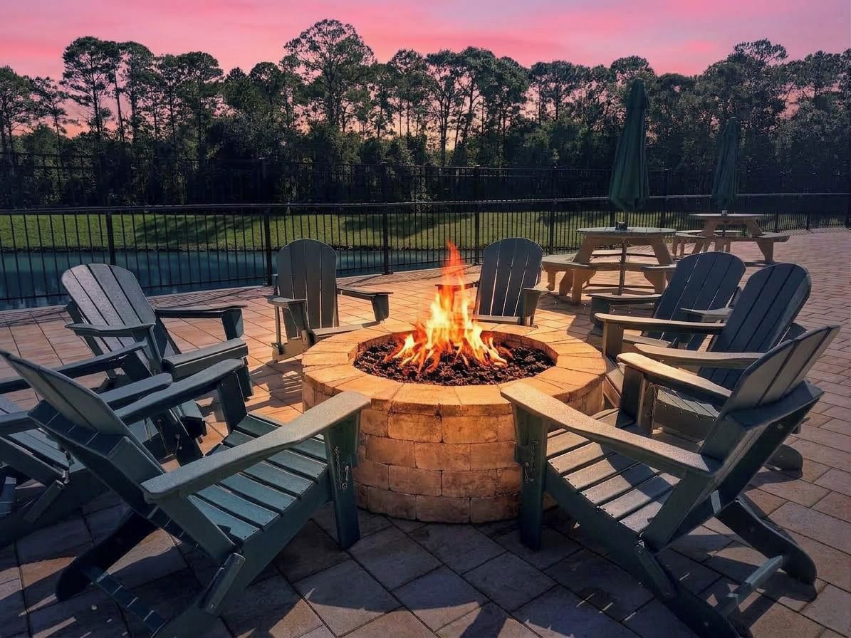 Un hogar de fuego rodeado de sillas Adirondack en un patio con vista a un campo de golf.