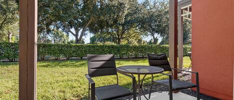 Un patio exterior con dos sillas y una mesa, rodeado de vegetación y un seto.
