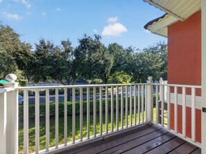 A wooden deck with a white railing, overlooking a green lawn and a road with parked cars. - PROMO Lovely 3 BR Villa, Resort Access - by Blue Sky Villas (Kissimmee)