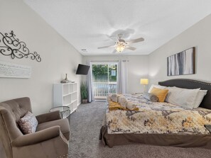 Une chambre à coucher comprenant un lit, une chaise, un bureau, un ventilateur de plafond, une télévision et une fenêtre donnant sur un paysage agréable.