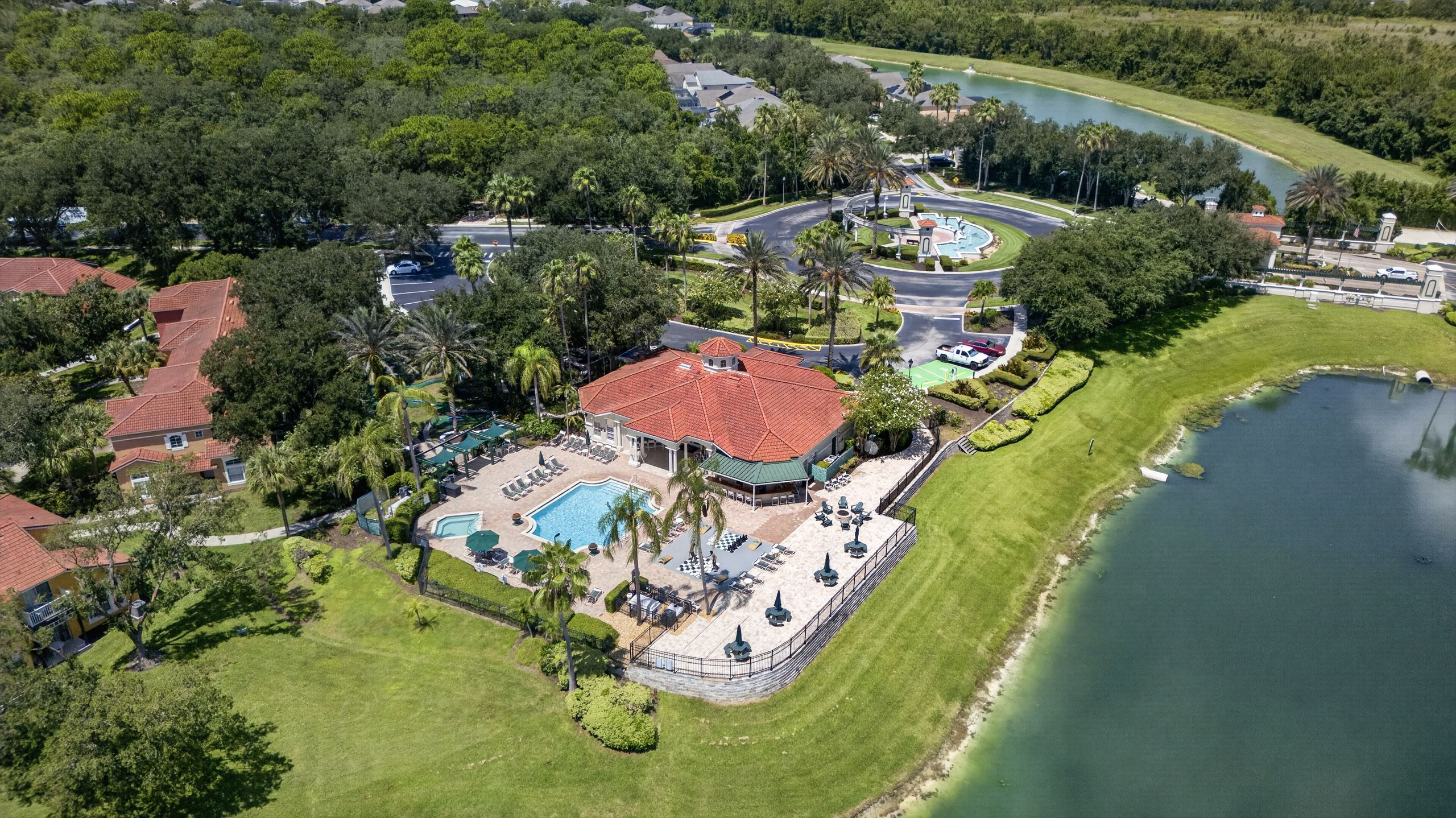 An aerial view of a residential area with a large house featuring a swimming pool, a tennis court, and a landscaped garden.