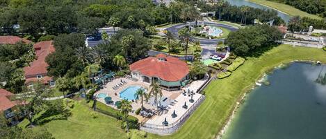 An aerial view of a residential area with a large house featuring a swimming pool, a tennis court, and a landscaped garden.