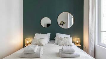 A hotel room with a bed, two bedside lamps, a large mirror, and a window.