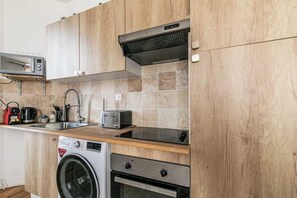 A compact kitchen with wooden cabinets, a built-in microwave, a toaster, a washing machine, and a dishwasher. - Charming Apartment - 2br/6p - Montreuil Near Paris (Montreuil)