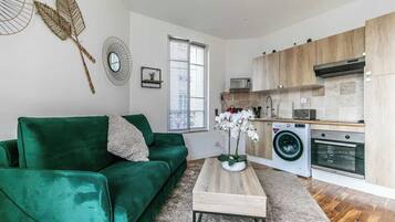 A compact living space with a green sofa, a coffee table, a washing machine, and a microwave in the kitchen area.