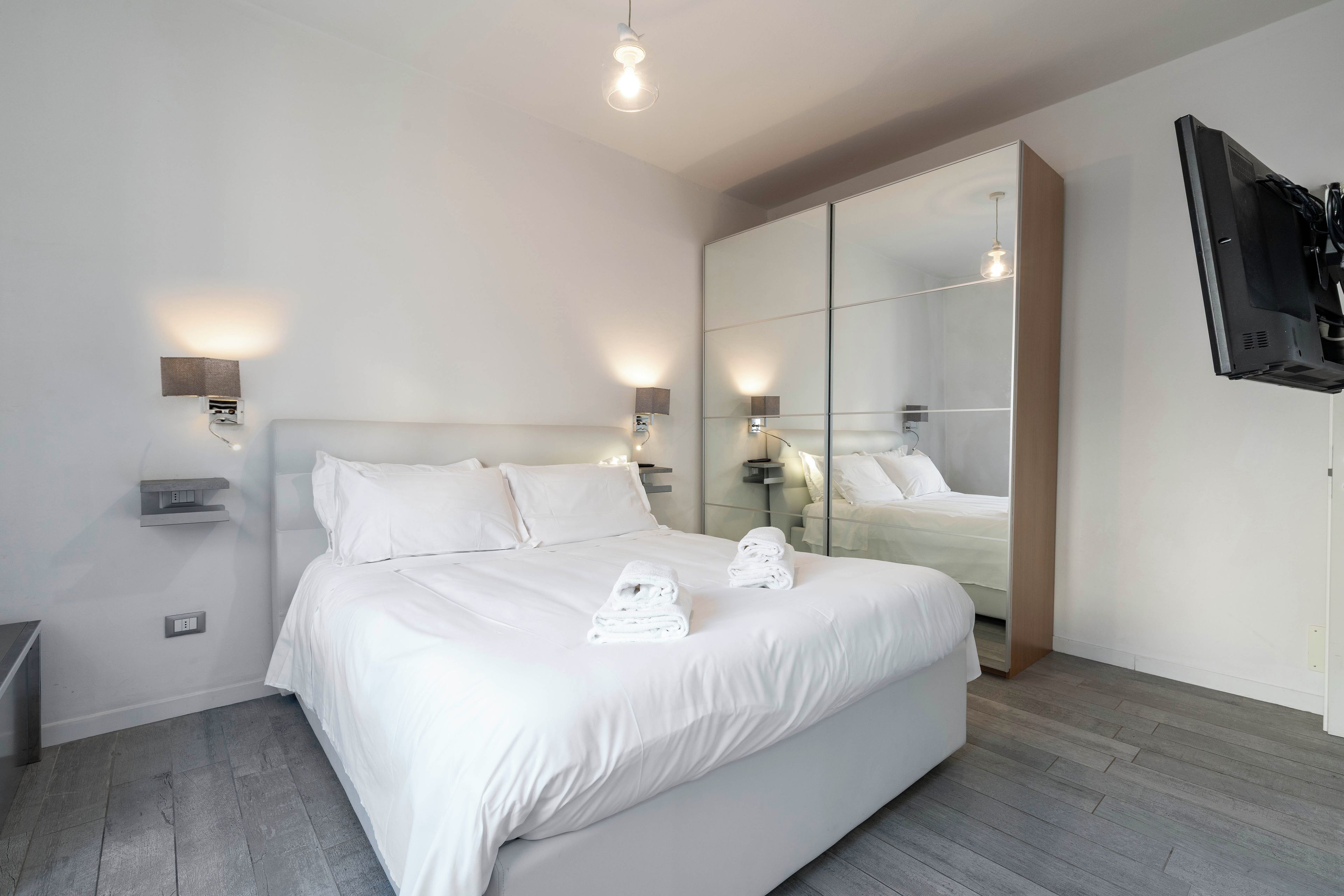 Habitación de hotel moderna con una cama grande, un armario, un televisor y una mesita de noche.