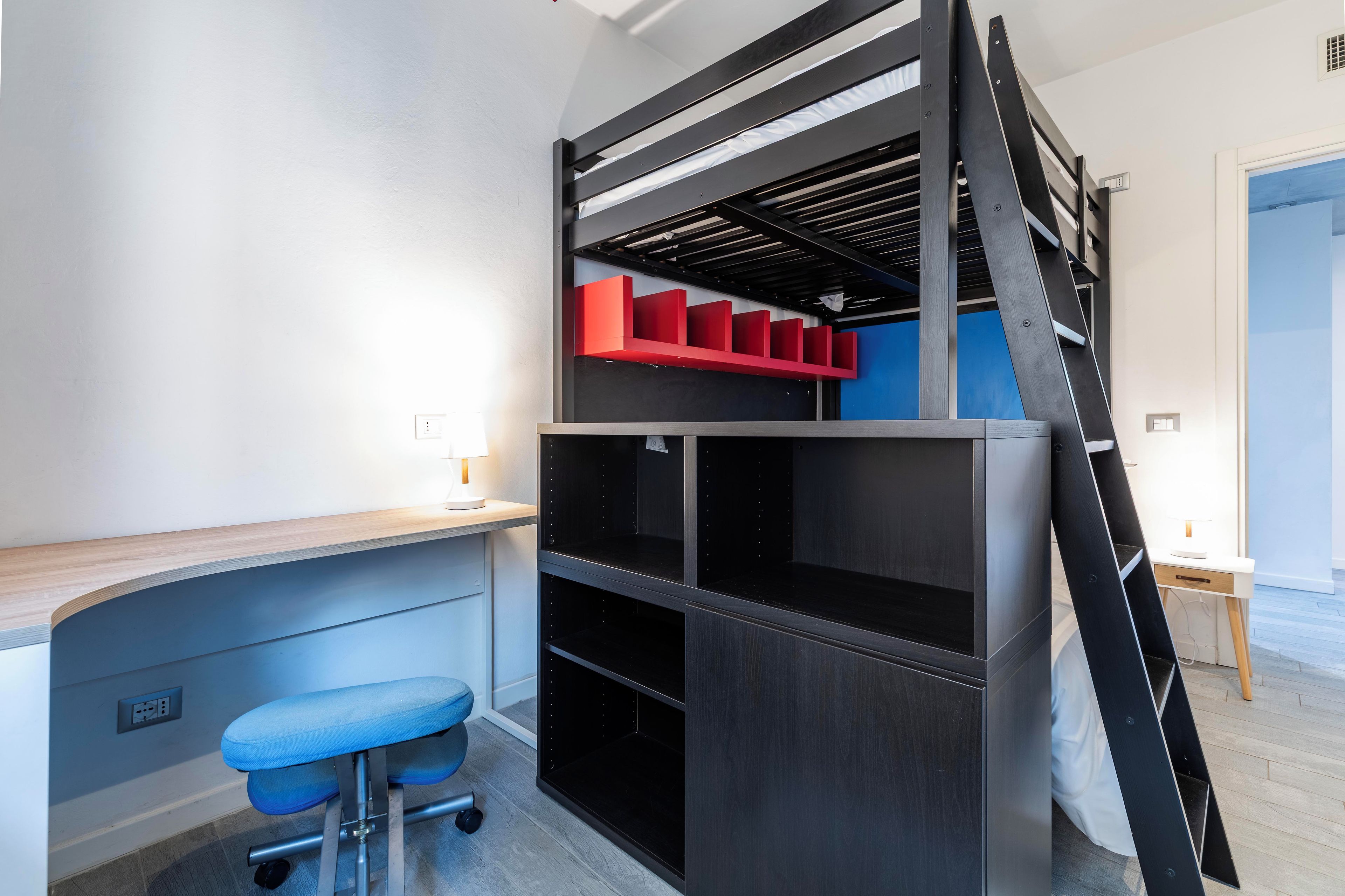 Un letto a castello con una scrivania, una sedia, una scala e un mobile contenitore rosso.