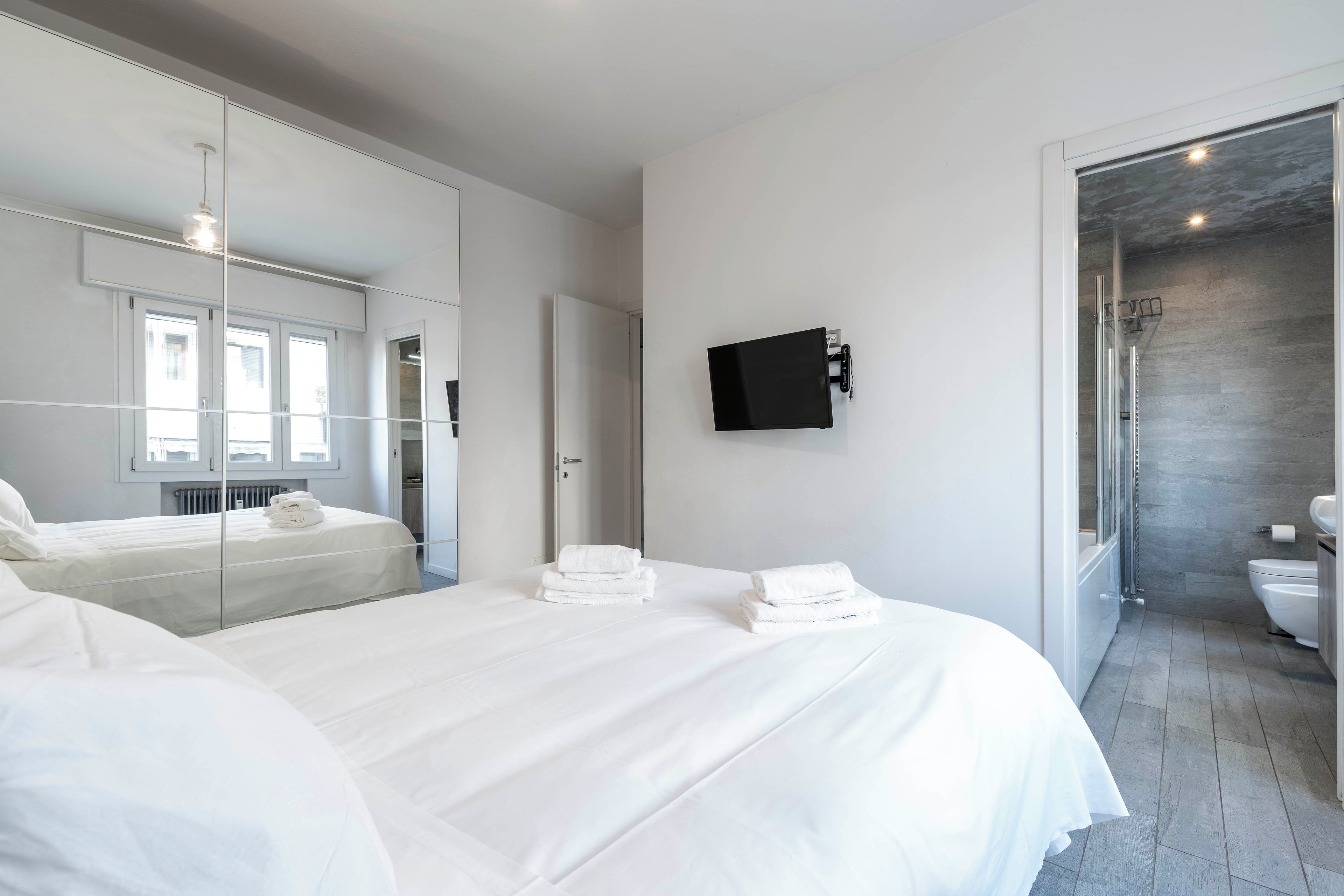 Ein modernes Hotelzimmer mit einem großen Bett, einem Flachbildfernseher und einem Badezimmer mit Dusche und Toilette.