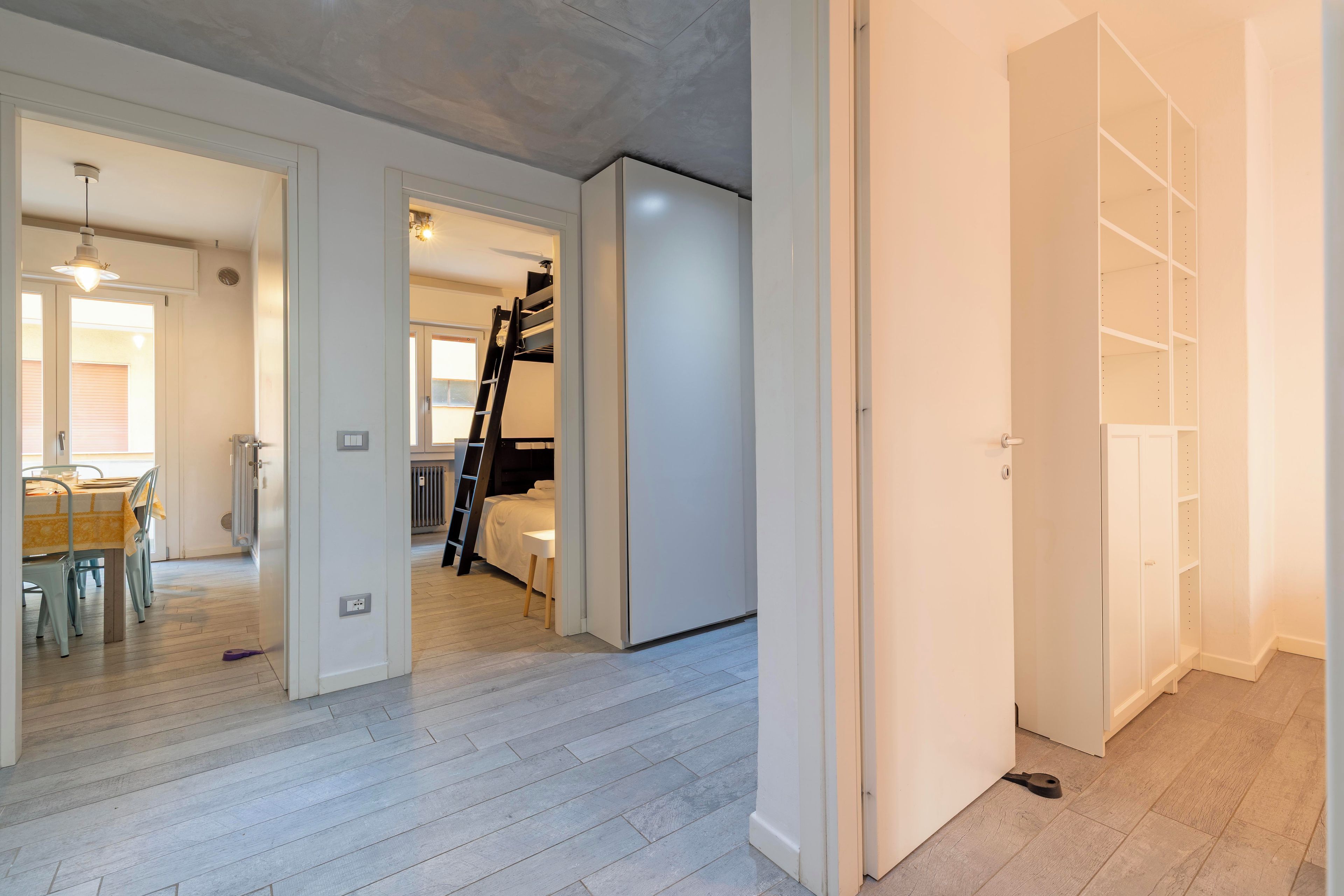Una habitación amplia con una cama litera, zona de comedor con mesa y sillas, y un vestidor con estantes.