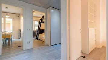 Una habitación amplia con una cama litera, zona de comedor con mesa y sillas, y un vestidor con estantes.