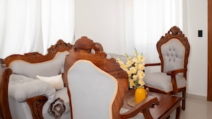 Ein Wohnzimmer mit einer Couch, einem Sessel und einem Couchtisch, einer Vase mit Blumen und Vorhängen.