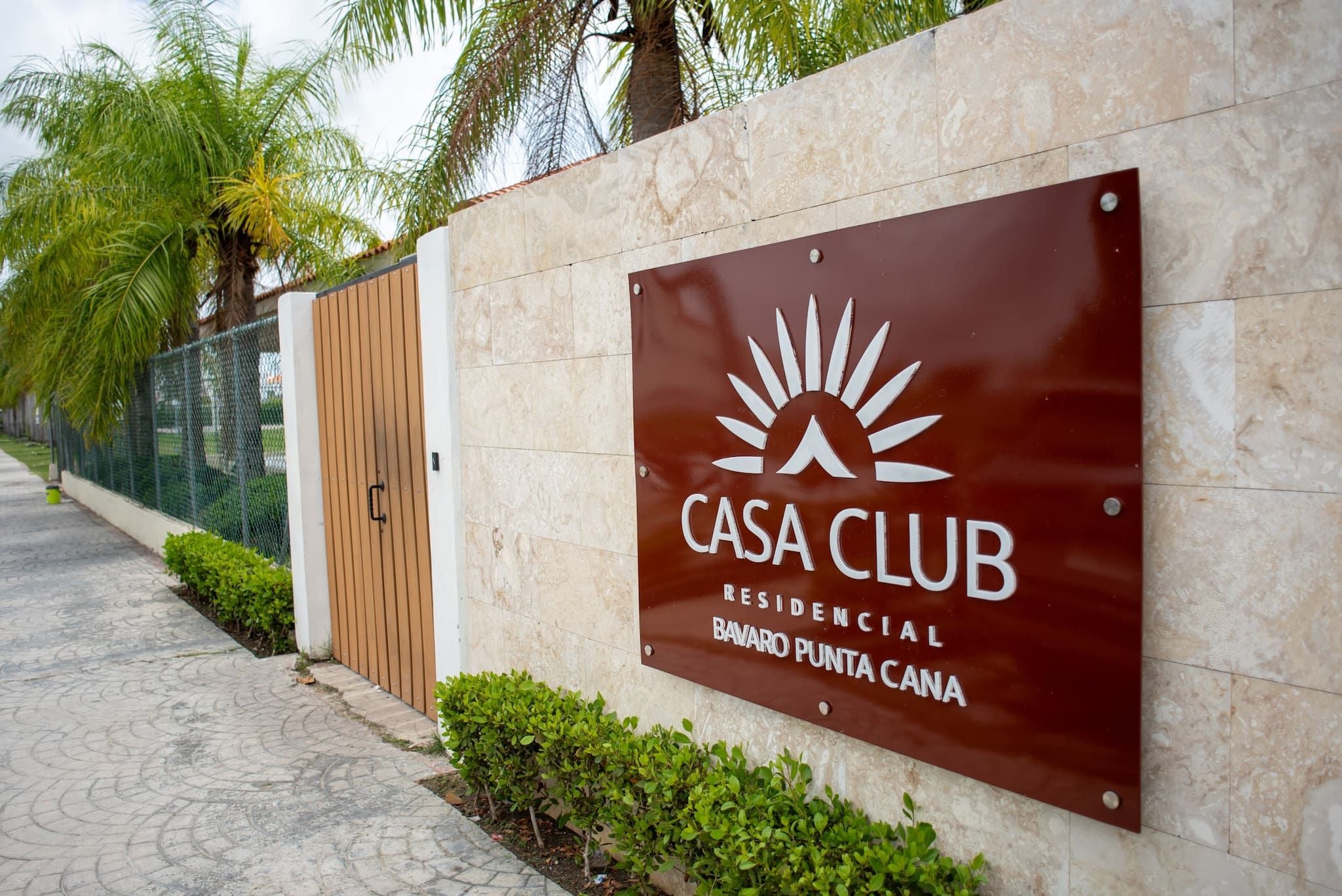 Laattaverhoilliseen seinään kiinnitetty kyltti, jossa lukee ”CASA CLUB RESIDENCIAL BAVARO PUNTA CANA” ja on aurinkosymboli.