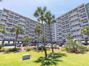 A multi-story hotel with balconies, palm trees, and a parking lot. - Pinnacle Port #A-306 - Two Waters Oasis | Near Beach + Amenities (Panama City Beach)
