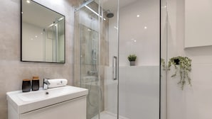 A modern bathroom with a glass-enclosed shower, a white sink with two decorative vases, and a potted plant on the wall. - Studio Wilcza with Parking  (Gdańsk)
