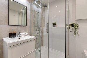 A modern bathroom with a glass-enclosed shower, a white sink with two decorative vases, and a potted plant on the wall. - Studio Wilcza with Parking  (Gdańsk)