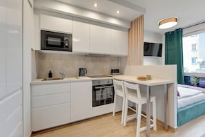 A compact kitchen with white cabinets, a microwave, oven, and a small dining area with a white chair. - Studio Wilcza with Parking  (Gdańsk)