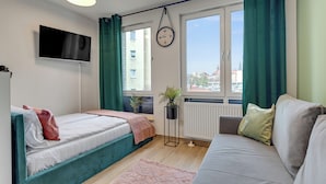 A modern bedroom with a bed, a sofa, a TV, a clock, and a window with curtains. - Studio Wilcza with Parking  (Gdańsk)