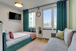 A modern bedroom with a bed, a sofa, a TV, a clock, and a window with curtains. - Studio Wilcza with Parking  (Gdańsk)