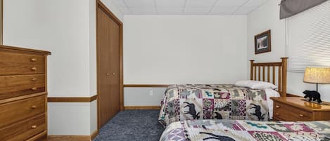 Ein Schlafzimmer mit einem Bett, einer Kommode, einem Nachttisch, einer Lampe, einem Deckenventilator und einem Fenster mit Jalousien.