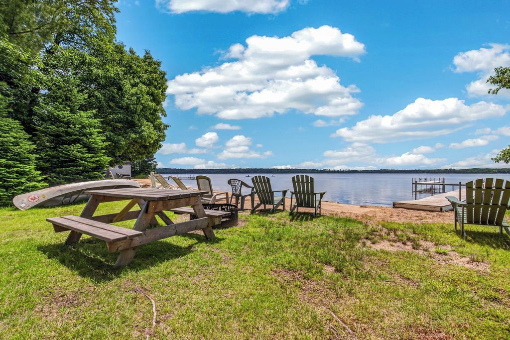 Un espace de pique-nique au bord du lac, avec une table et des chaises en bois, une pelouse en premier plan et une vue sur le lac et la rive éloignée.