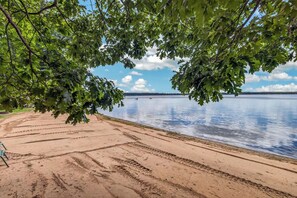 A sandy beach with footprints leading to the water, surrounded by trees. - Stepaway Vacation Rentals/Hillcrest Cottages-Cedar Lodge (Saint Germain)