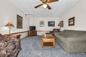 A living room with a ceiling fan, a television, a sofa, a coffee table, and framed pictures on the walls. - Stepaway Vacation Rentals/Hillcrest Cottages-Cedar Lodge (Saint Germain)