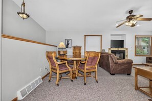 A living room with a round wooden table, four chairs, a brown sofa, a ceiling fan, a television, and a fireplace. - Stepaway Vacation Rentals/Hillcrest Cottages-Cedar Lodge (Saint Germain)