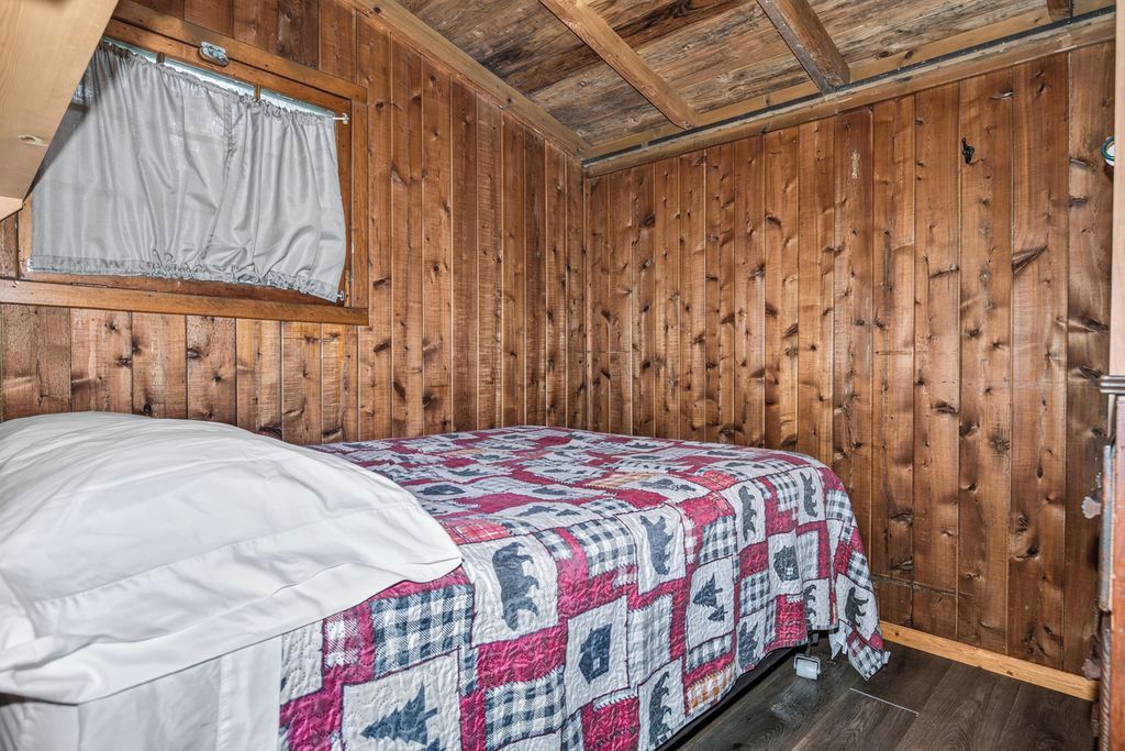 A single bed with a quilt in a room with wooden walls and a sloped ceiling.
