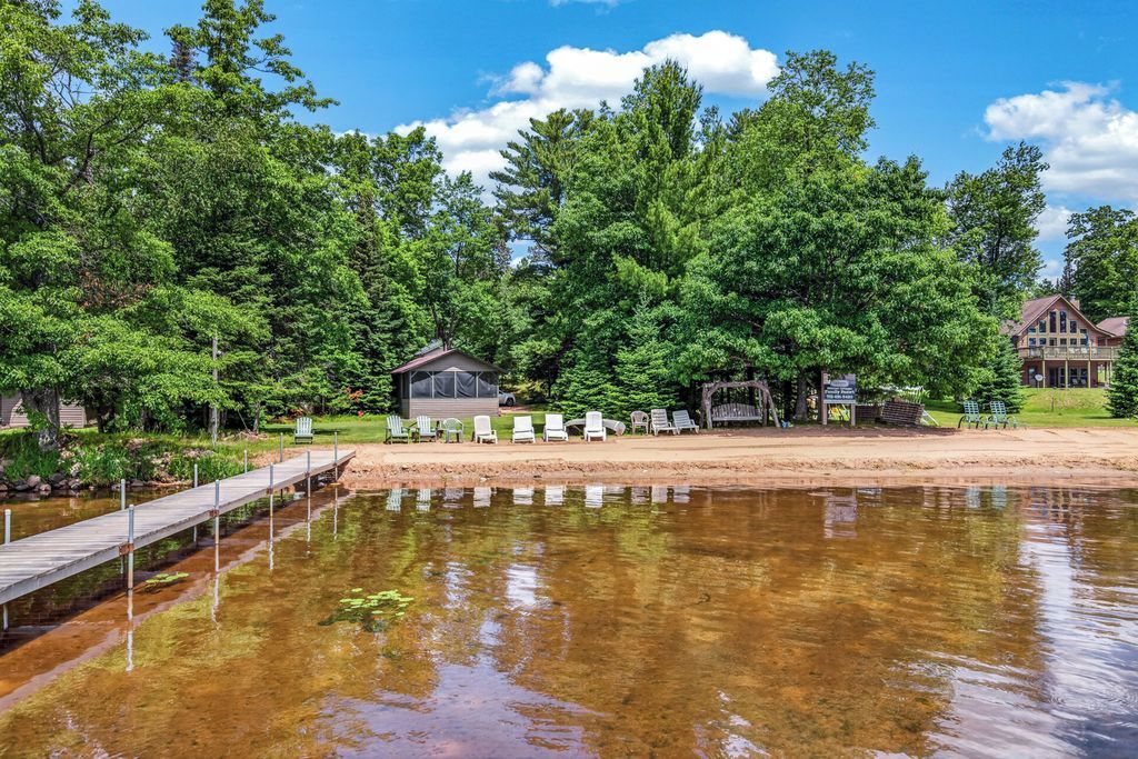 A lakeside property with a wooden dock, a covered seating area, and a large house with a porch.