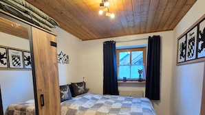 Ett sovrum med ett träpanelat tak, en säng med ett mönstrat överkast, ett fönster med gardiner och dekorationer på väggarna.
