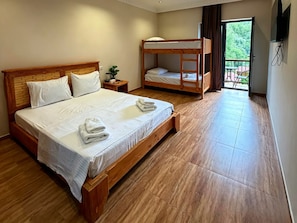 A hotel room with a large bed, a smaller bunk bed, a nightstand with a plant, and a balcony with outdoor furniture. - Sonat Resort (Gosh)