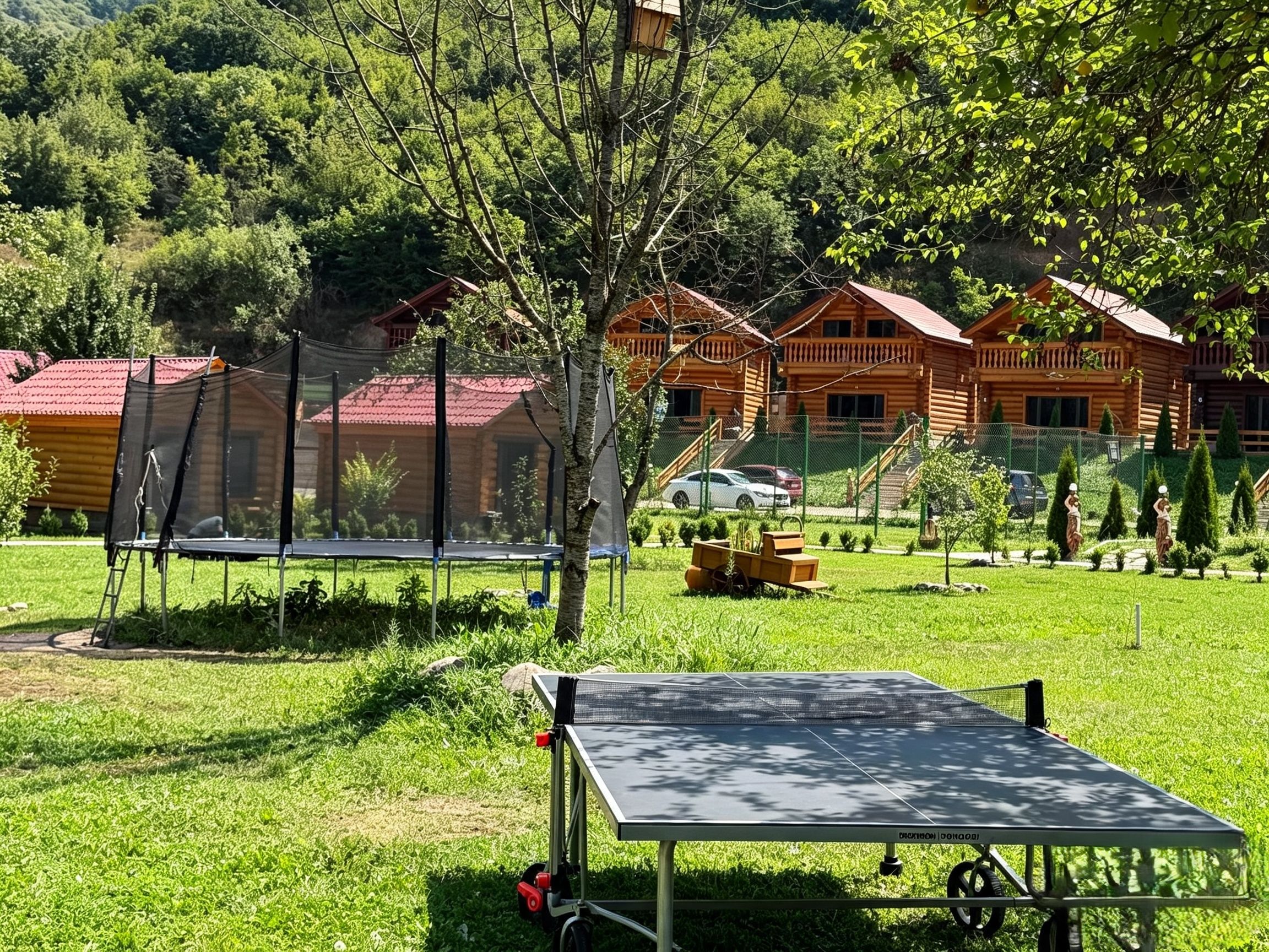 A wooden cabin with a red roof, surrounded by lush greenery and a trampoline.
