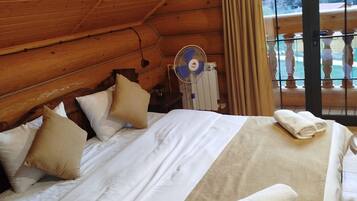 Un dormitorio de cabaña de madera con cama, almohadas, un ventilador y vistas por una ventana.