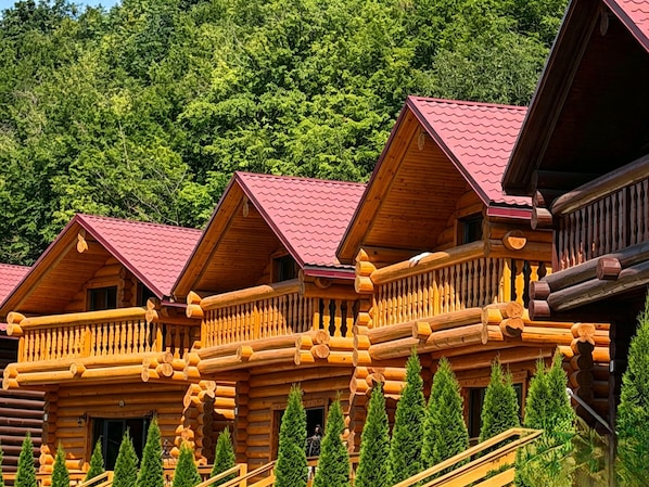 A row of log cabins with balconies, surrounded by evergreen trees.