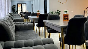Uma sala de jantar moderna com assentos estofados em cinza, cadeiras com pés dourados e um relógio de parede.