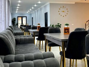 A modern dining area with grey upholstered seating, gold-legged chairs, and a wall clock. - Sonat Resort (Gosh)