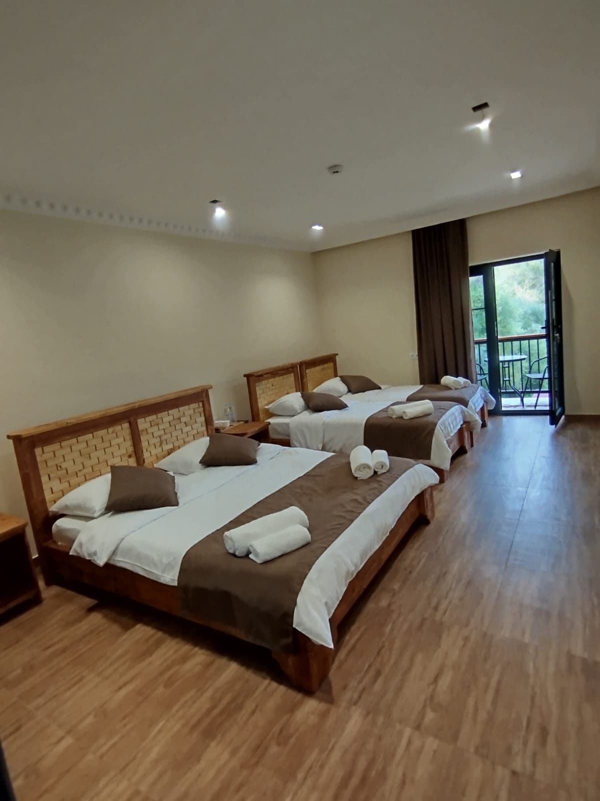 Habitación de hotel con cuatro camas dispuestas en fila, un balcón con sillas y suelo de madera.