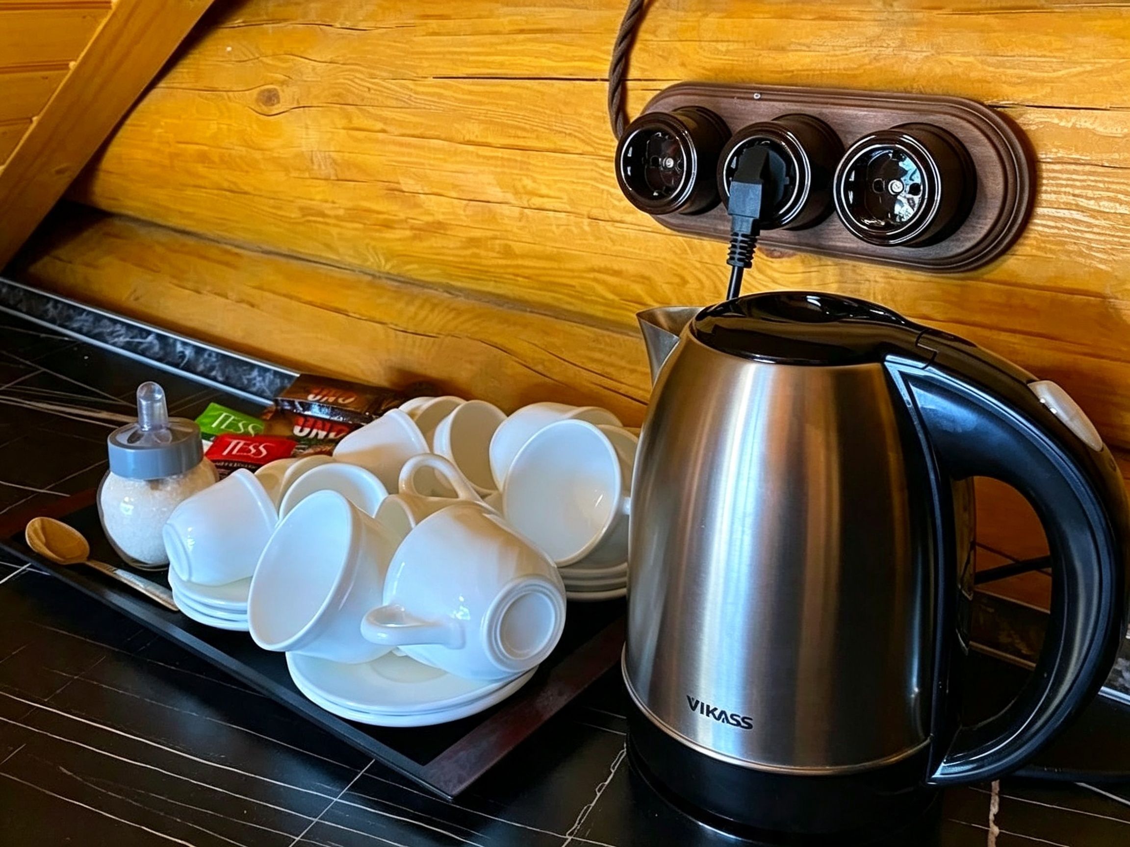 A stainless steel electric kettle on a stove, a set of white cups, and a box of tea bags.