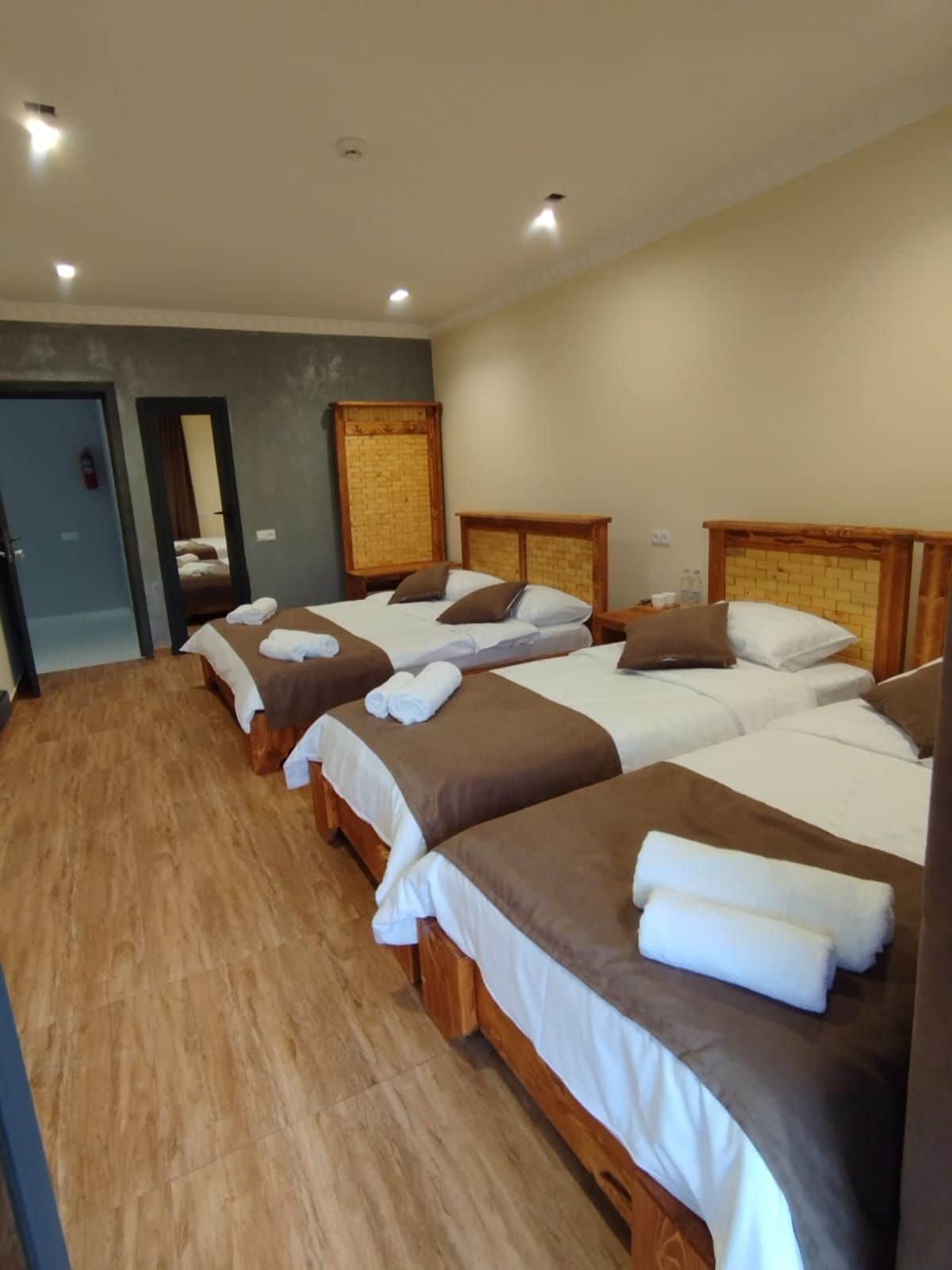 Ein Hotelzimmer mit vier Einzelbetten, jeweils mit einem hölzernen Kopfteil und weißer Bettwäsche.
