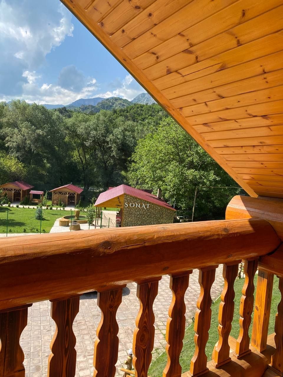 Barandilla de madera con vista a un paisaje montañoso con varias construcciones de techo rojo.