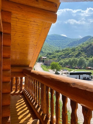 A wooden balcony with a view of a mountainous landscape and a road with vehicles.