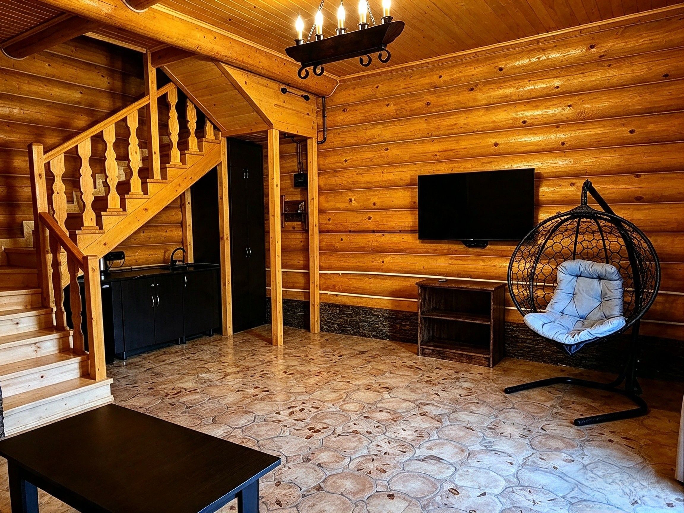A wooden interior with a staircase, a flat-screen TV mounted on the wall, a hanging chair, and a small table.