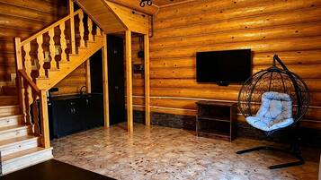 A wooden interior with a staircase, a flat-screen TV mounted on the wall, a hanging chair, and a small table.