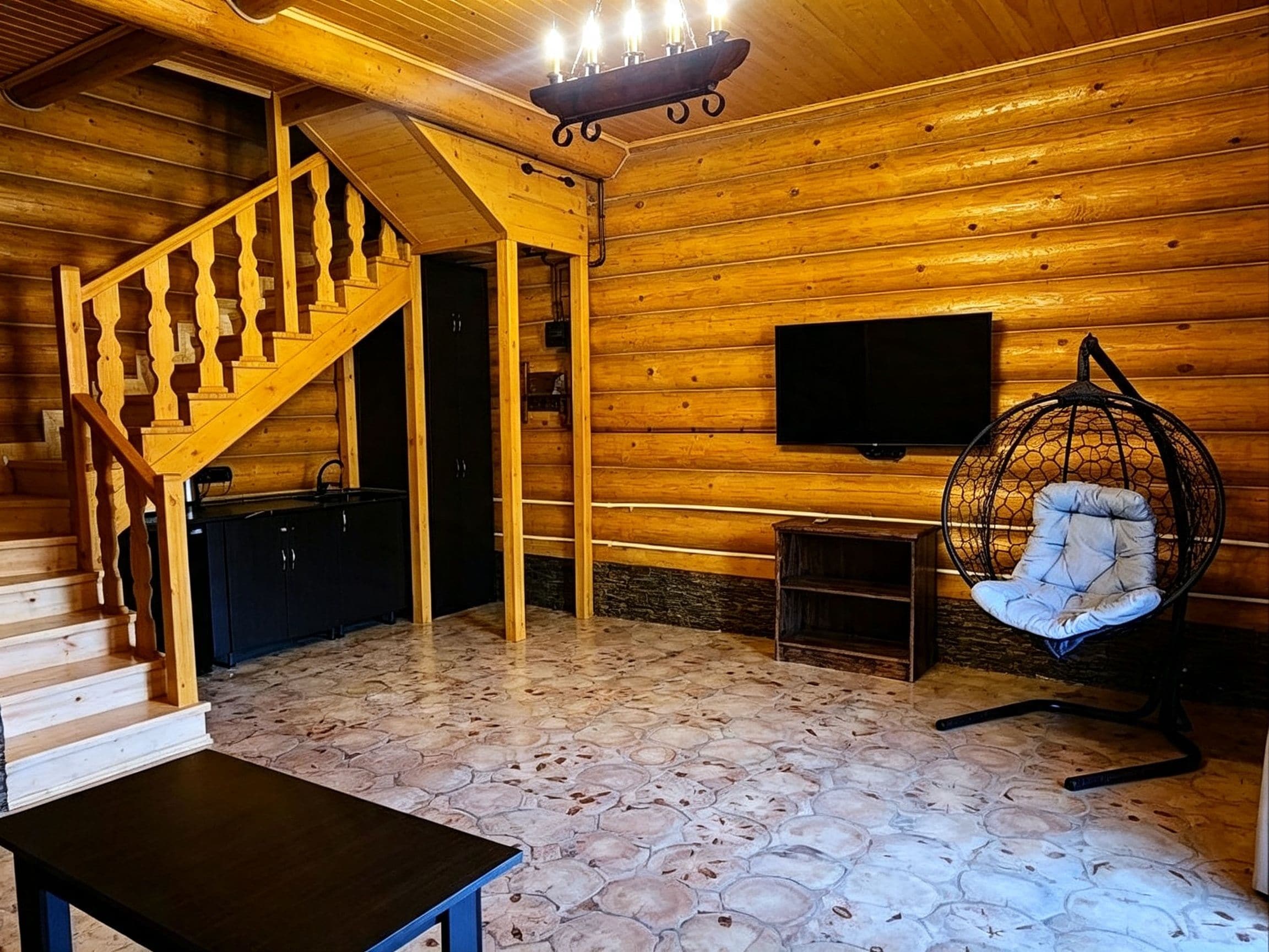 A wooden interior with a staircase, a television mounted on the wall, a hanging chair, and a small table.