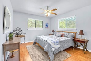 A bedroom with a bed, bedside tables, a ceiling fan, and windows. - Hidden Creek Hideaway | Hot Tub, 2 Acres & Near Jacob's Well (Wimberley)
