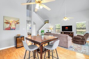 A modern living room with a dining area, a sofa, a TV, and a ceiling fan. - Hidden Creek Hideaway | Hot Tub, 2 Acres & Near Jacob's Well (Wimberley)