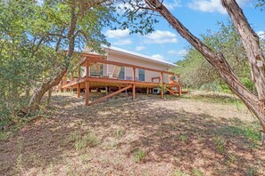 A house with a wooden deck, surrounded by trees and a clear sky. - Hidden Creek Hideaway | Hot Tub, 2 Acres & Near Jacob's Well (Wimberley)